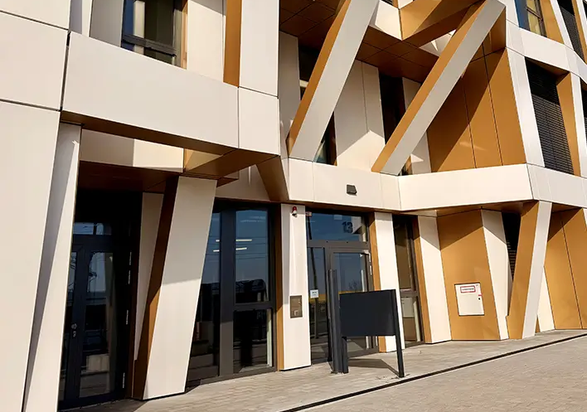 Detailansicht des Eingangsbereichs der Brainfactory Bochum mit markanter Fassadenstruktur, schrägen Stützelementen und moderner Architektur in Weiß- und Goldtönen.