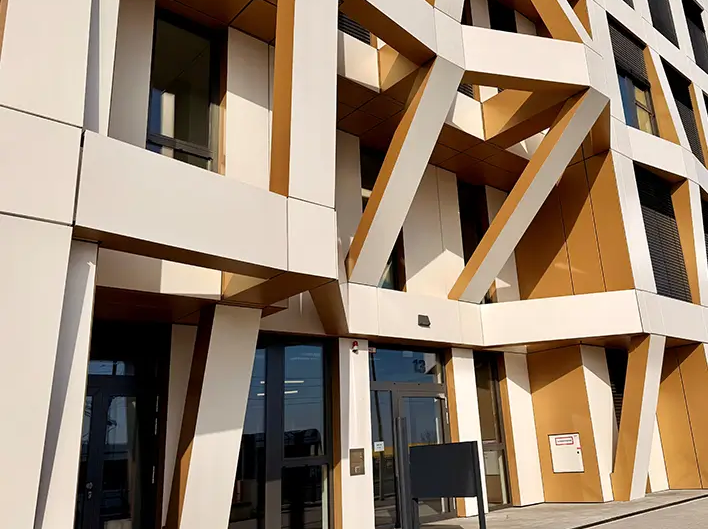 Detailansicht des Eingangsbereichs der Brainfactory Bochum mit markanter Fassadenstruktur, schrägen Stützelementen und moderner Architektur in Weiß- und Goldtönen.